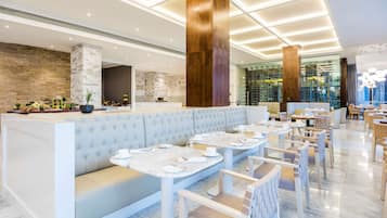 A modern restaurant with a long white bench, round tables, and a stone wall.