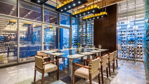 A modern restaurant with a long table set for dining, surrounded by glass walls and shelves of wine bottles. - Hyatt Regency San Luis Potosi (San Luis Potosi)