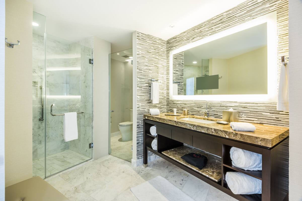 A modern bathroom with a glass shower enclosure, a large mirror, and a marble countertop.