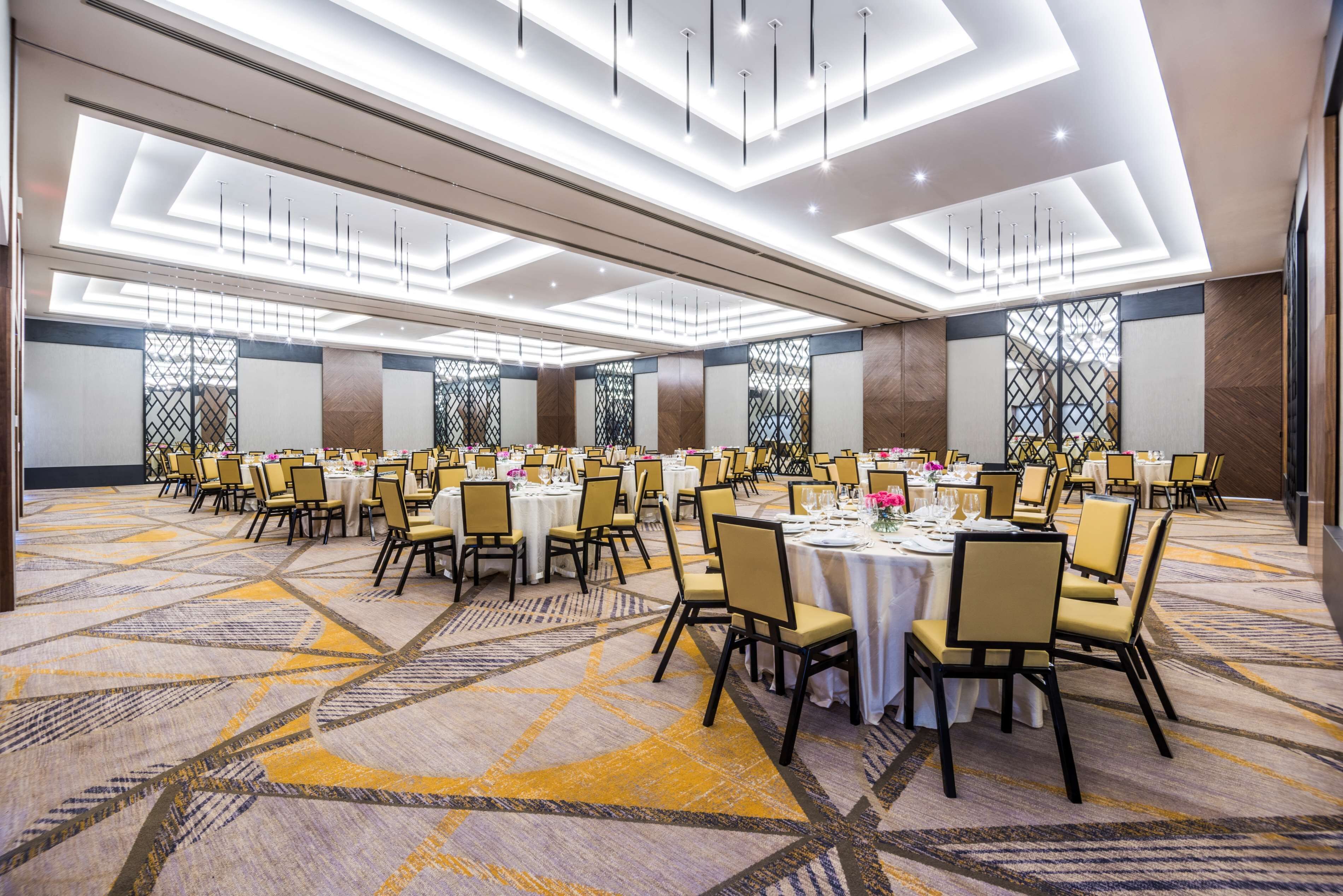 Une grande salle de banquet avec de nombreuses tables rondes, chacune recouverte d’une nappe blanche et entourée de chaises.
