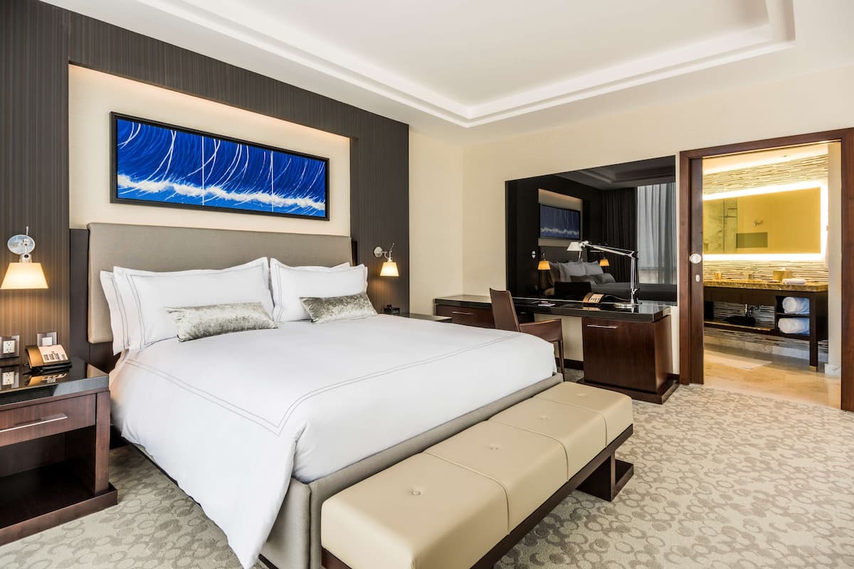A hotel room with a large bed, bedside tables, a desk, and a bathroom visible through an open door.