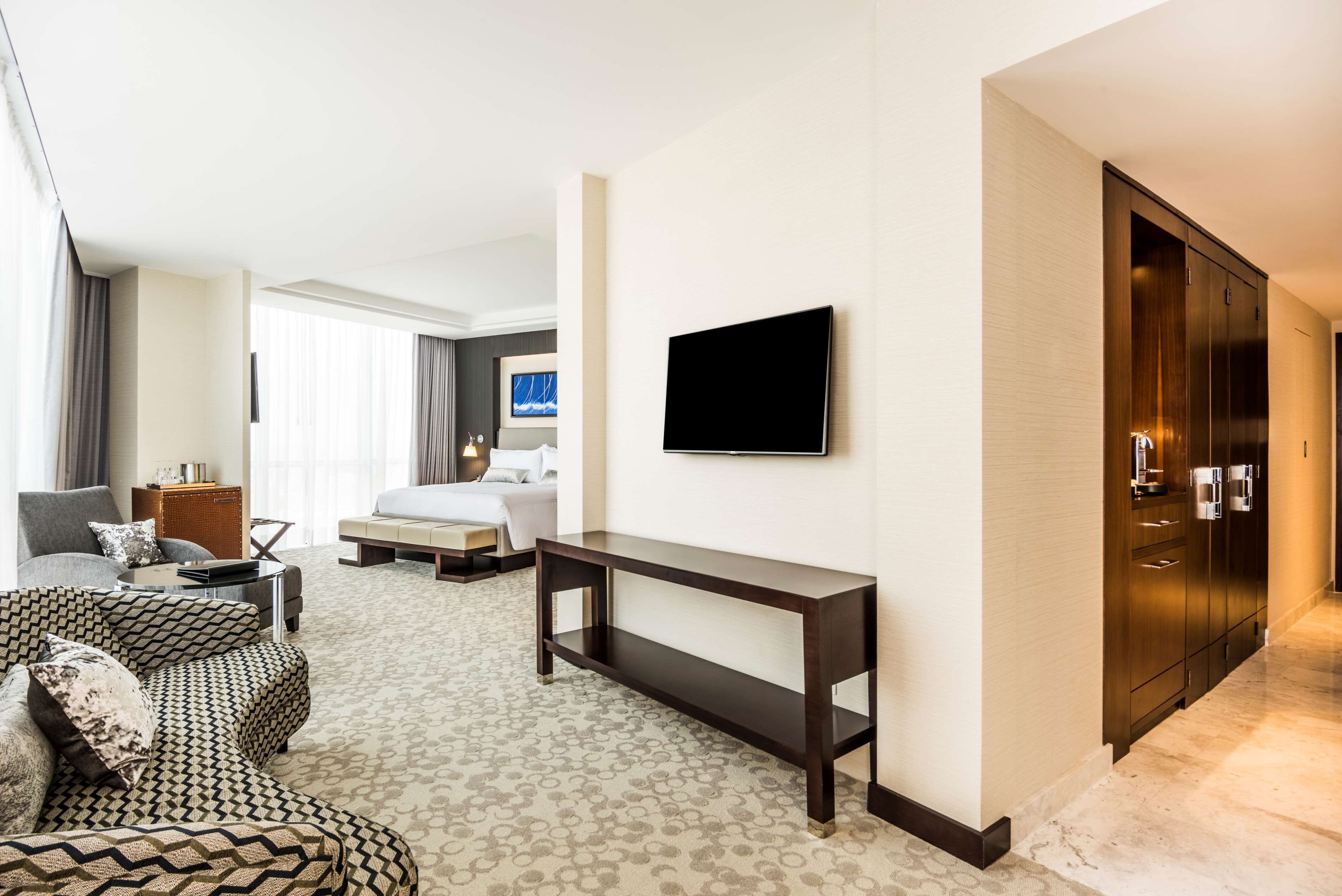 Una habitación de hotel con sofá, cama, televisor, mesa consola y armario.