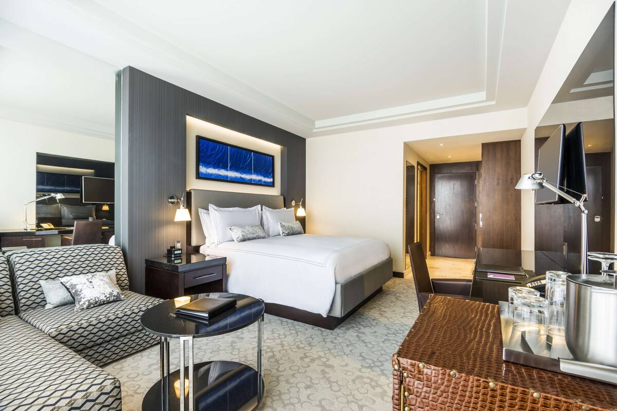 A hotel room with a large bed, a sofa, a small table, and a TV mounted on the wall.