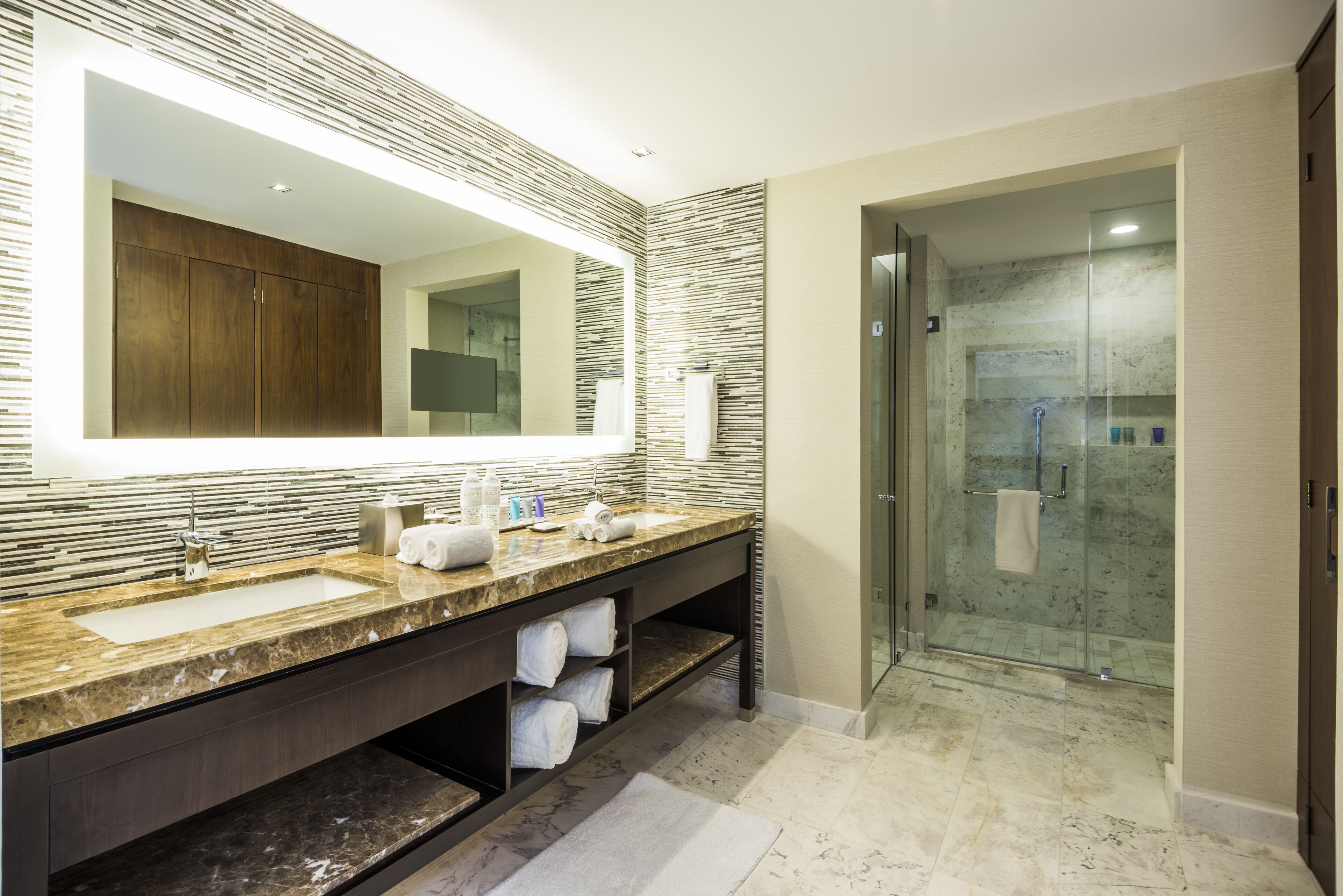 A modern bathroom with a large mirror, dual sinks, a shower, and a marble countertop.