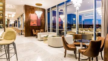 A modern lounge area with seating arrangements, large windows, and contemporary lighting fixtures.