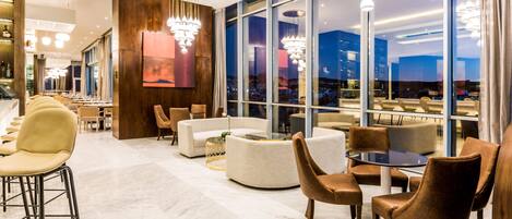 A modern lounge area with seating arrangements, large windows, and contemporary lighting fixtures.