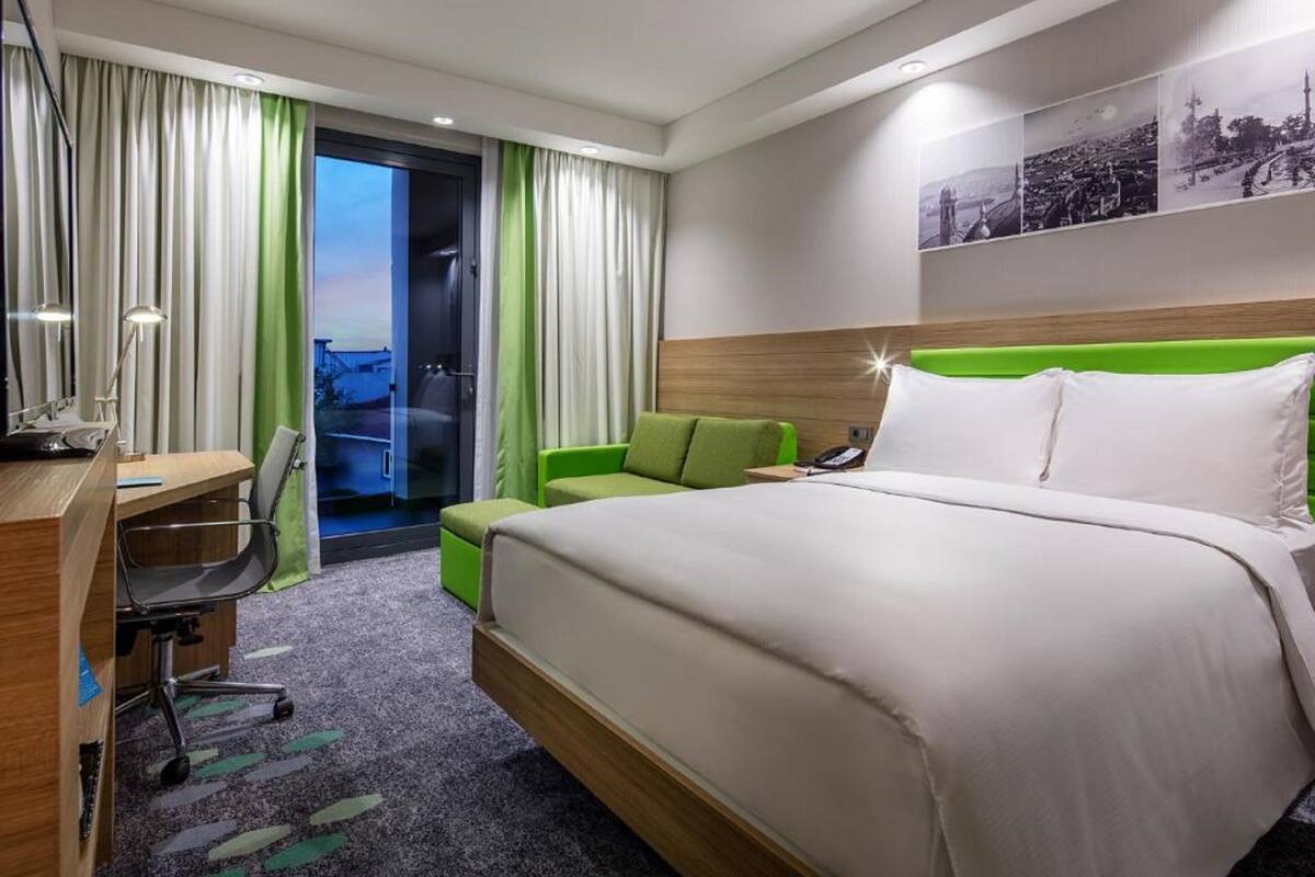 Une chambre d’hôtel avec un lit, un bureau, une chaise et un canapé vert.