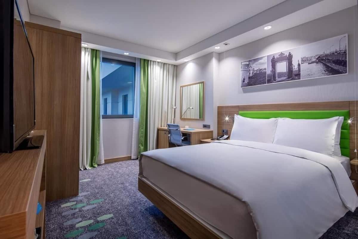 Une chambre d’hôtel avec un lit, un bureau, une chaise et une grande fenêtre avec des rideaux.