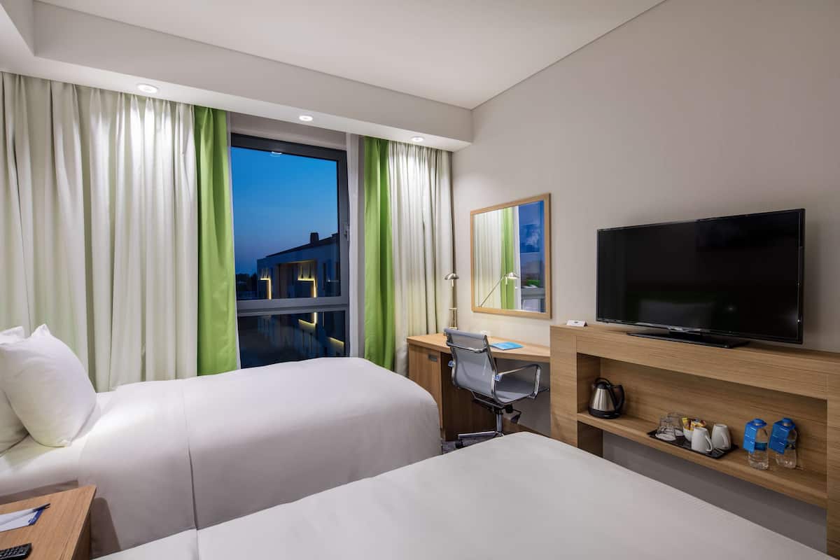 Une chambre d’hôtel avec deux lits, un bureau, une télévision et une fenêtre avec des rideaux.