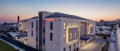 Un moderno hotel Hampton con techo plano, ventanas amplias y una entrada bien iluminada.