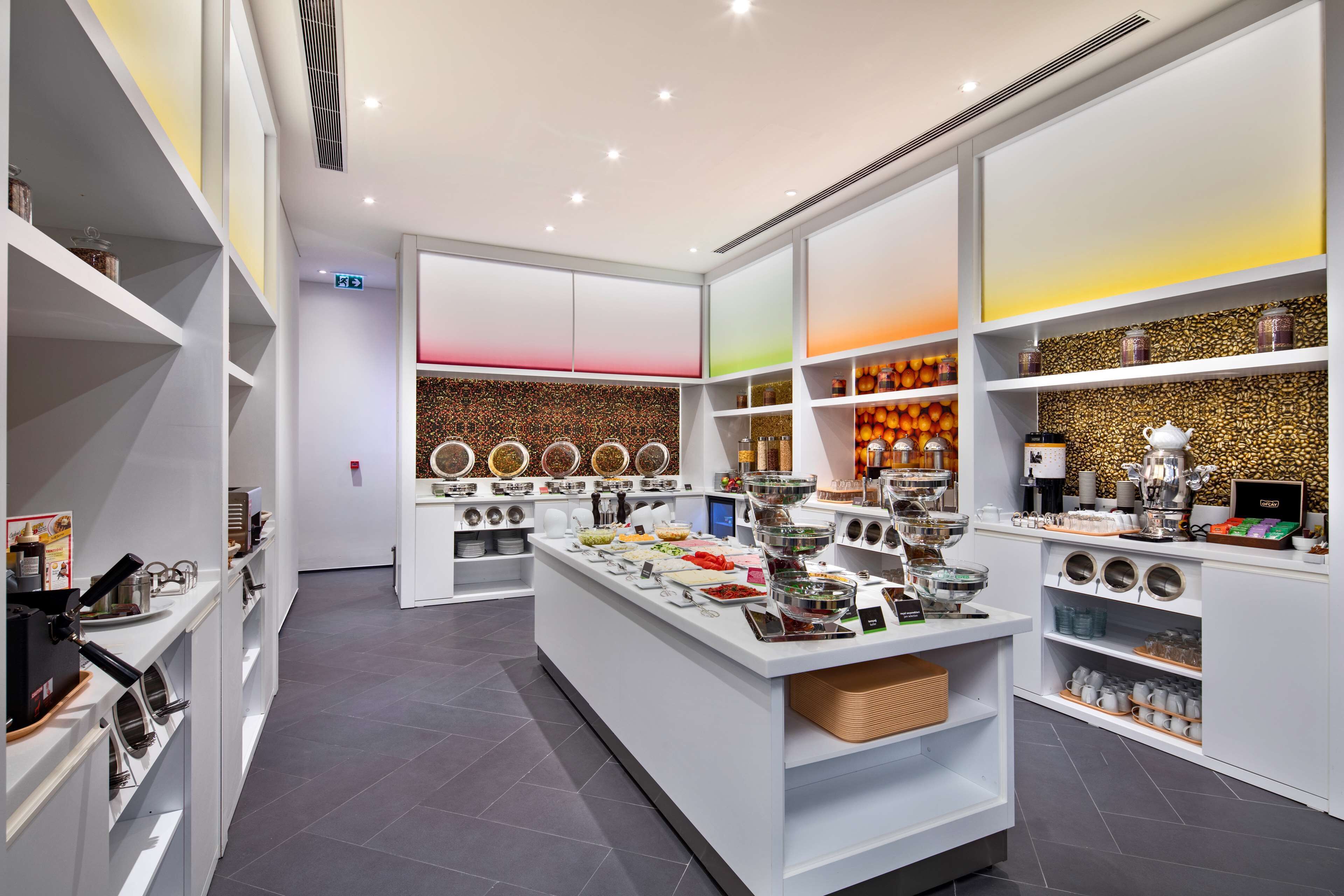 A modern kitchen area with white cabinetry, a central island with food items, and shelves with kitchenware.