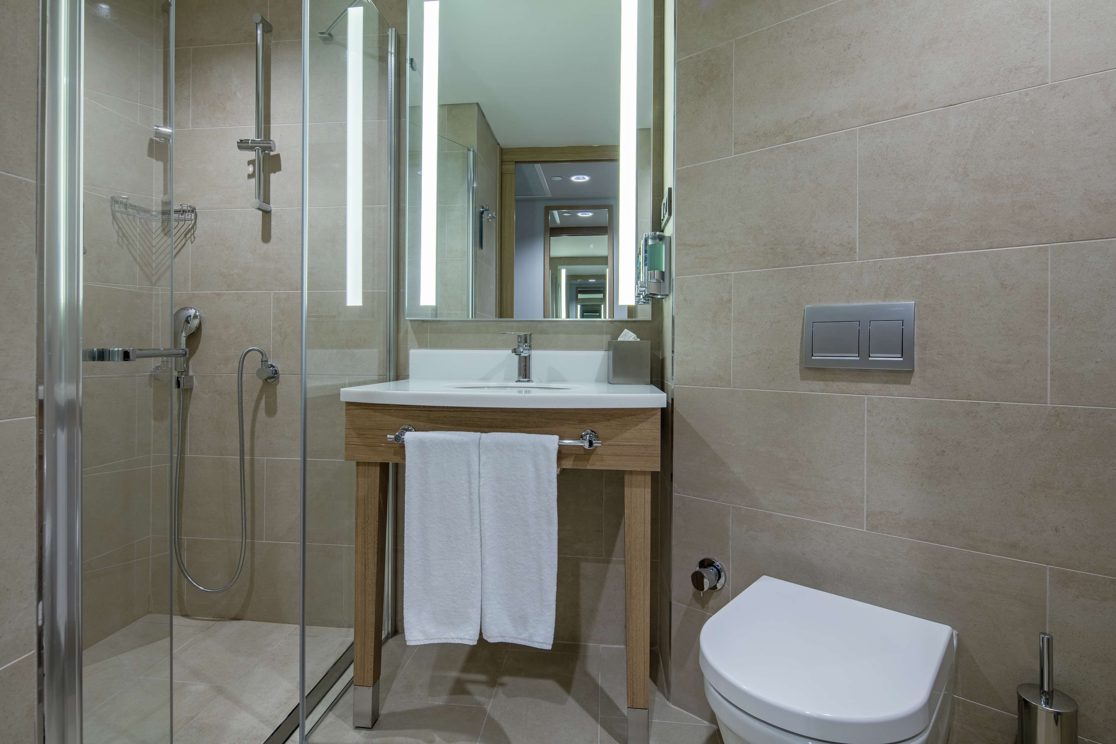 A modern bathroom with a glass-enclosed shower, a wooden vanity with a white sink, and a white toilet.