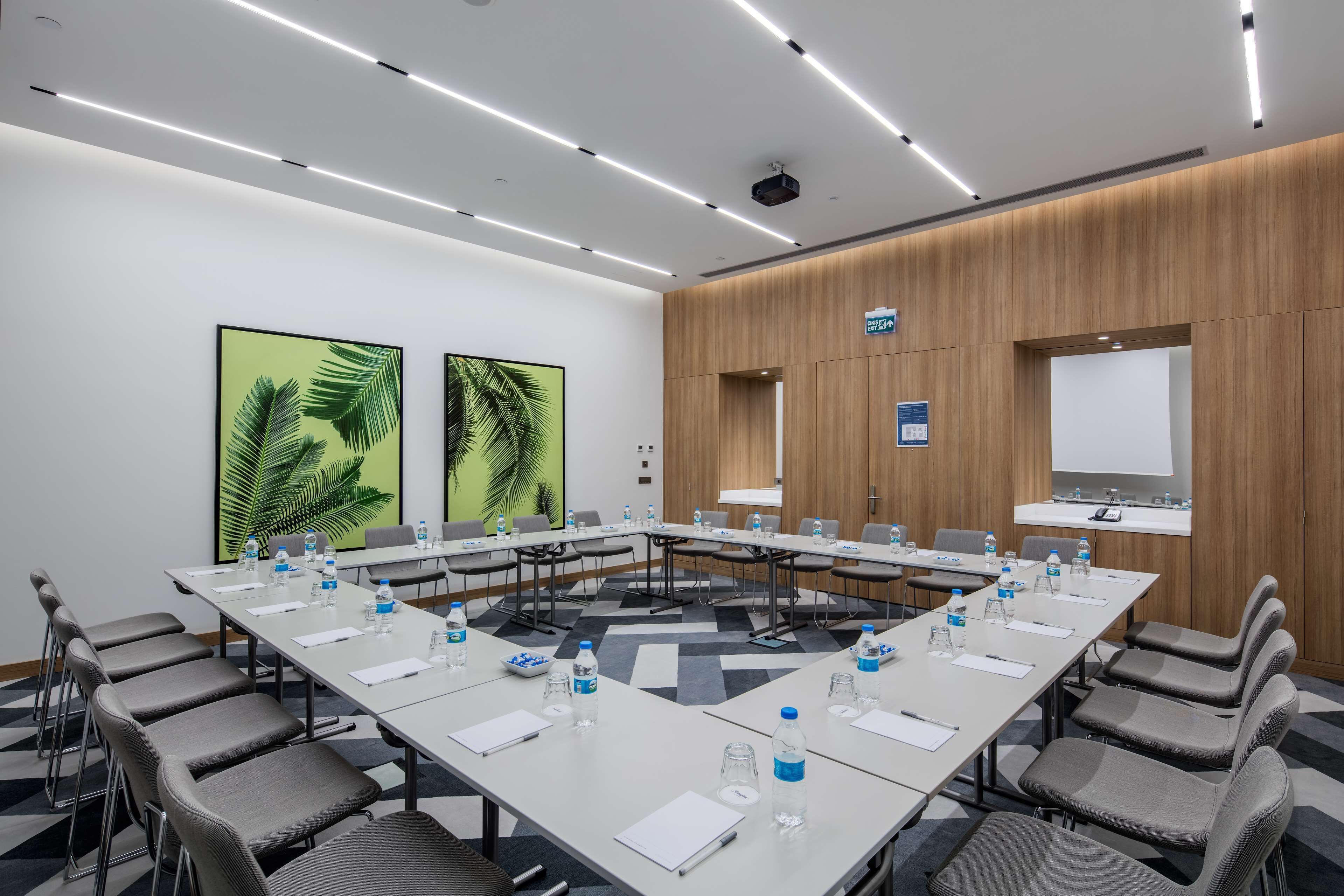 A conference room with a long table, chairs, water bottles, and a projector screen.