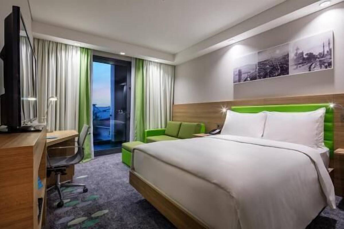 A hotel room with a bed, a desk, a chair, and a television.