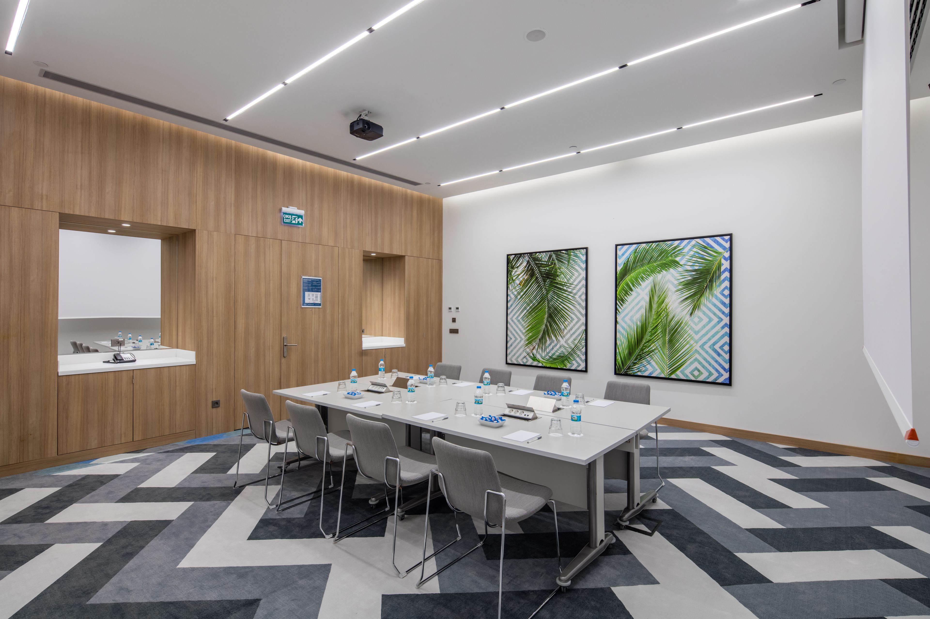 Un salón de conferencias con una larga mesa, sillas, una pizarra y dos obras de arte enmarcadas en la pared.