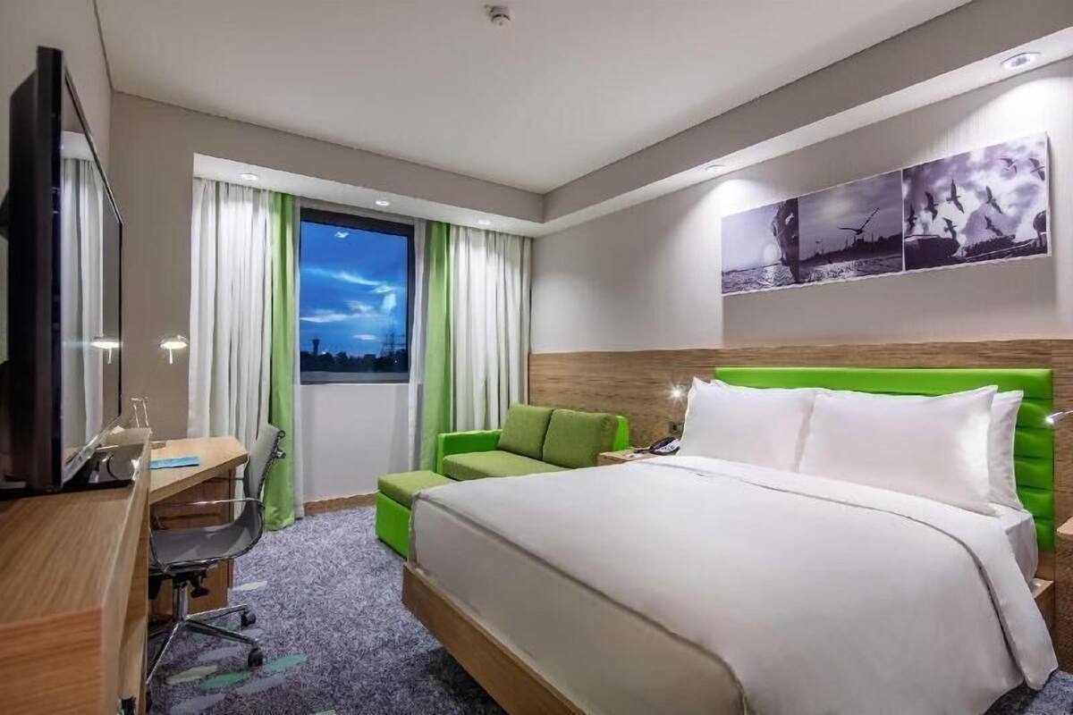 A hotel room with a bed, a desk, a chair, a TV, and a window with curtains.