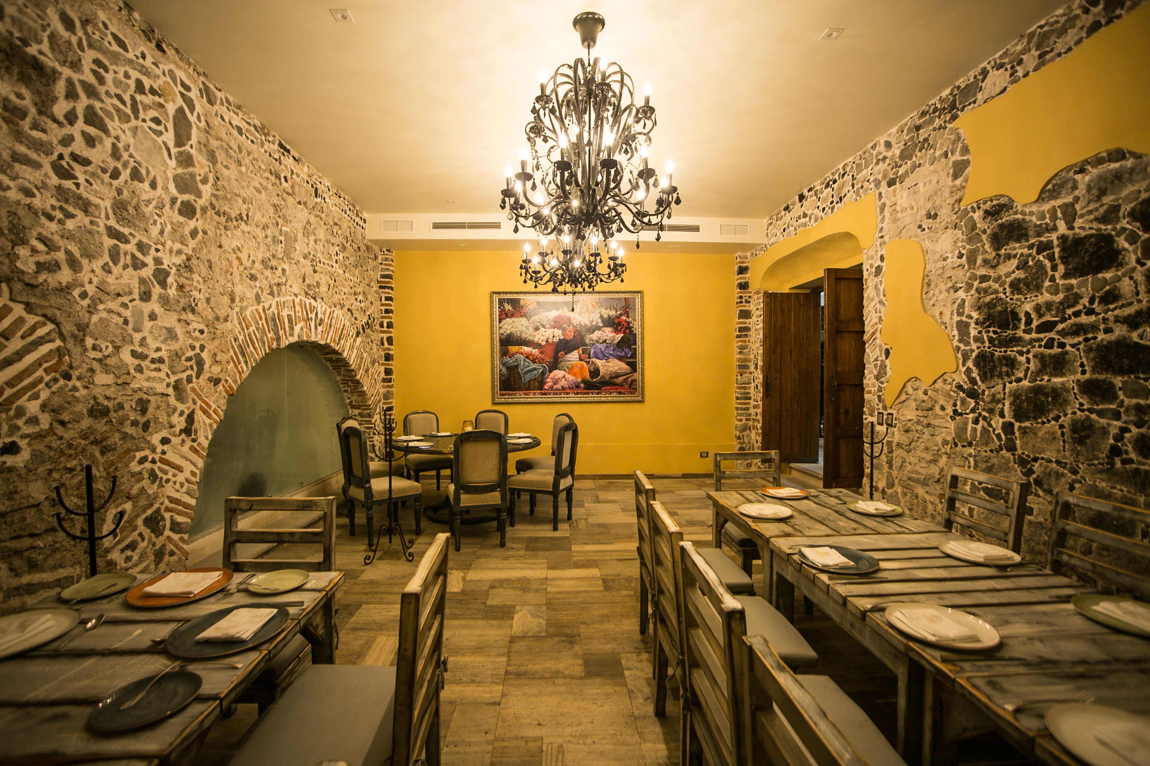 Un comedor con paredes de piedra, una araña y un cuadro en la pared.