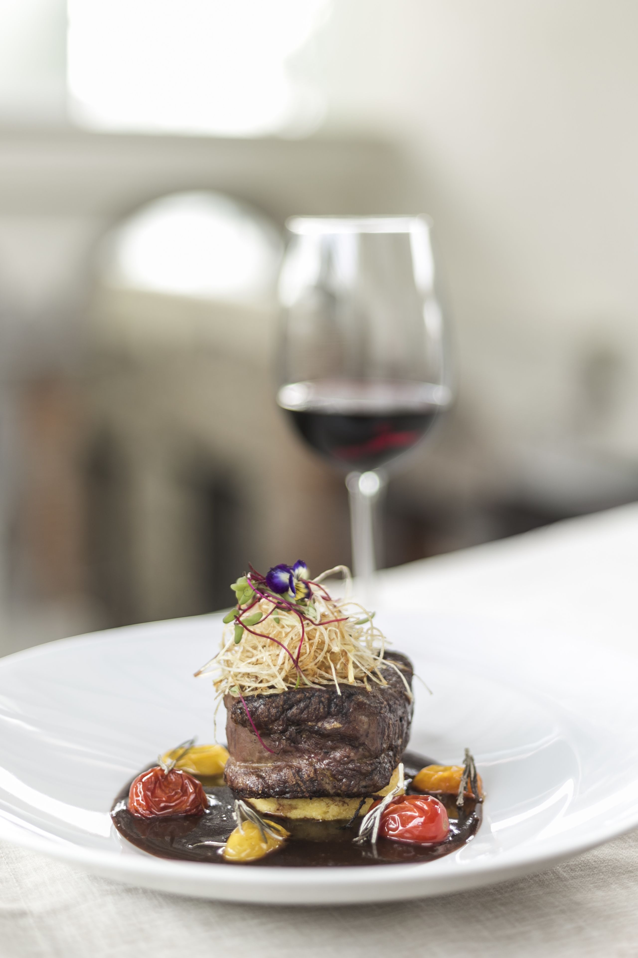 Un plato de carne con vegetales y una copa de vino tinto.