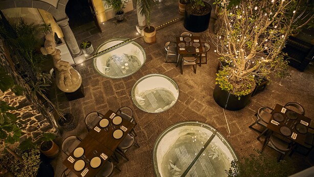An indoor courtyard with multiple round tables and chairs, surrounded by potted plants and a statue. - Casona de los Sapos Hotel Boutique (Puebla)