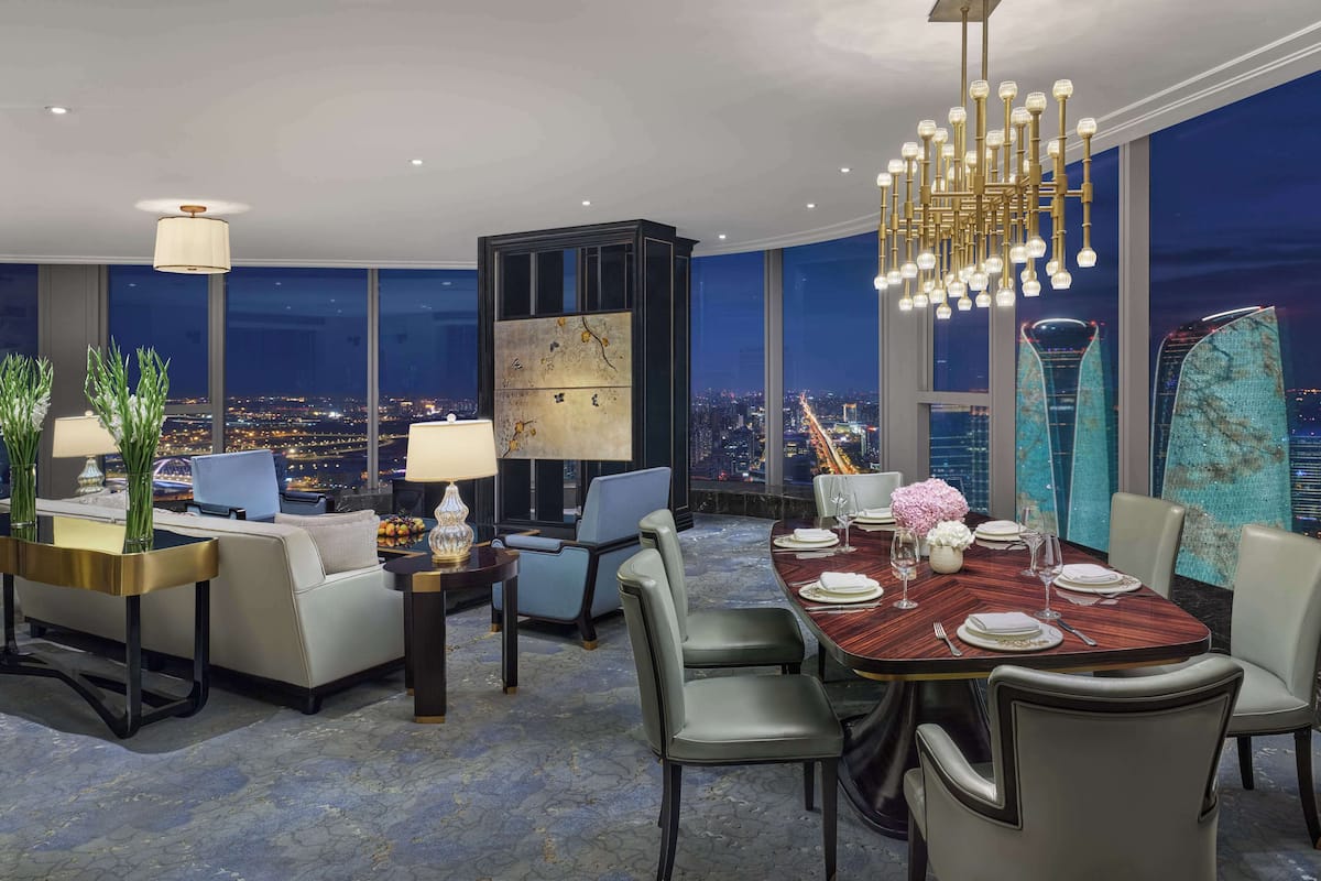 A modern dining area with a city view, a chandelier, and a large abstract painting.