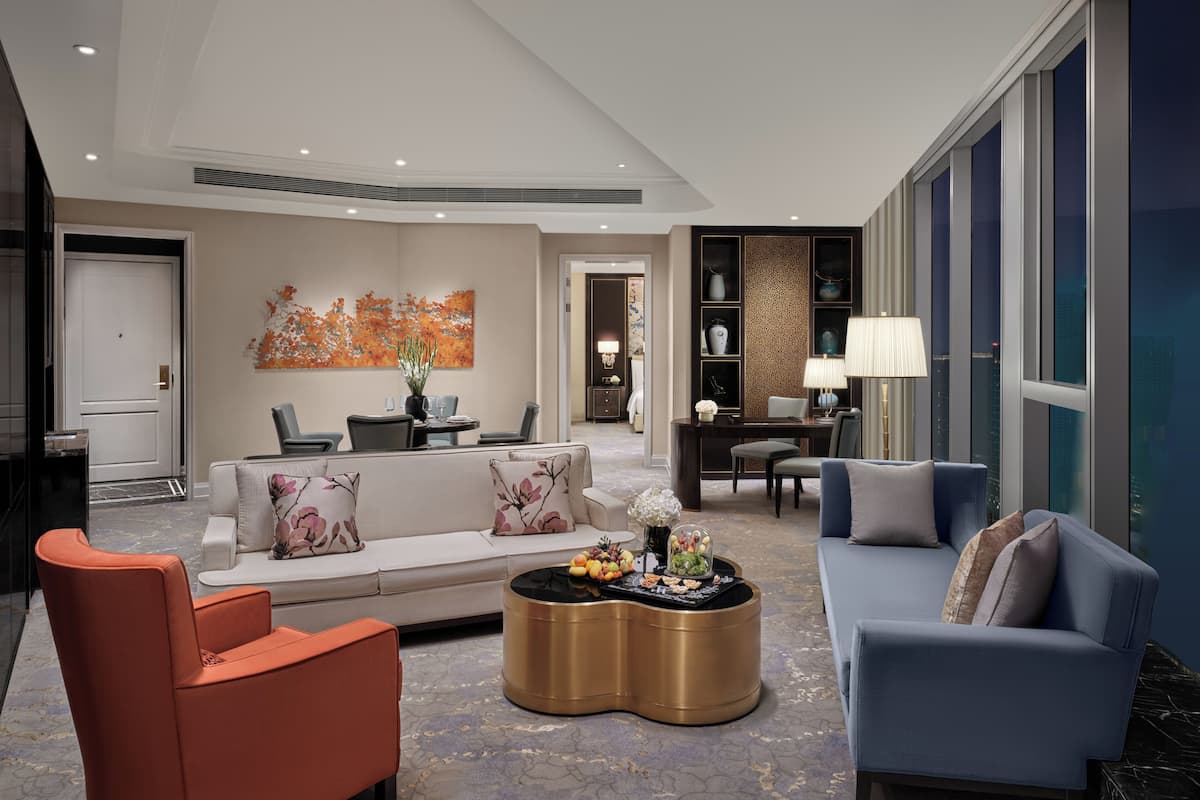 A modern hotel lobby with a sofa, armchairs, a coffee table, and a dining area.