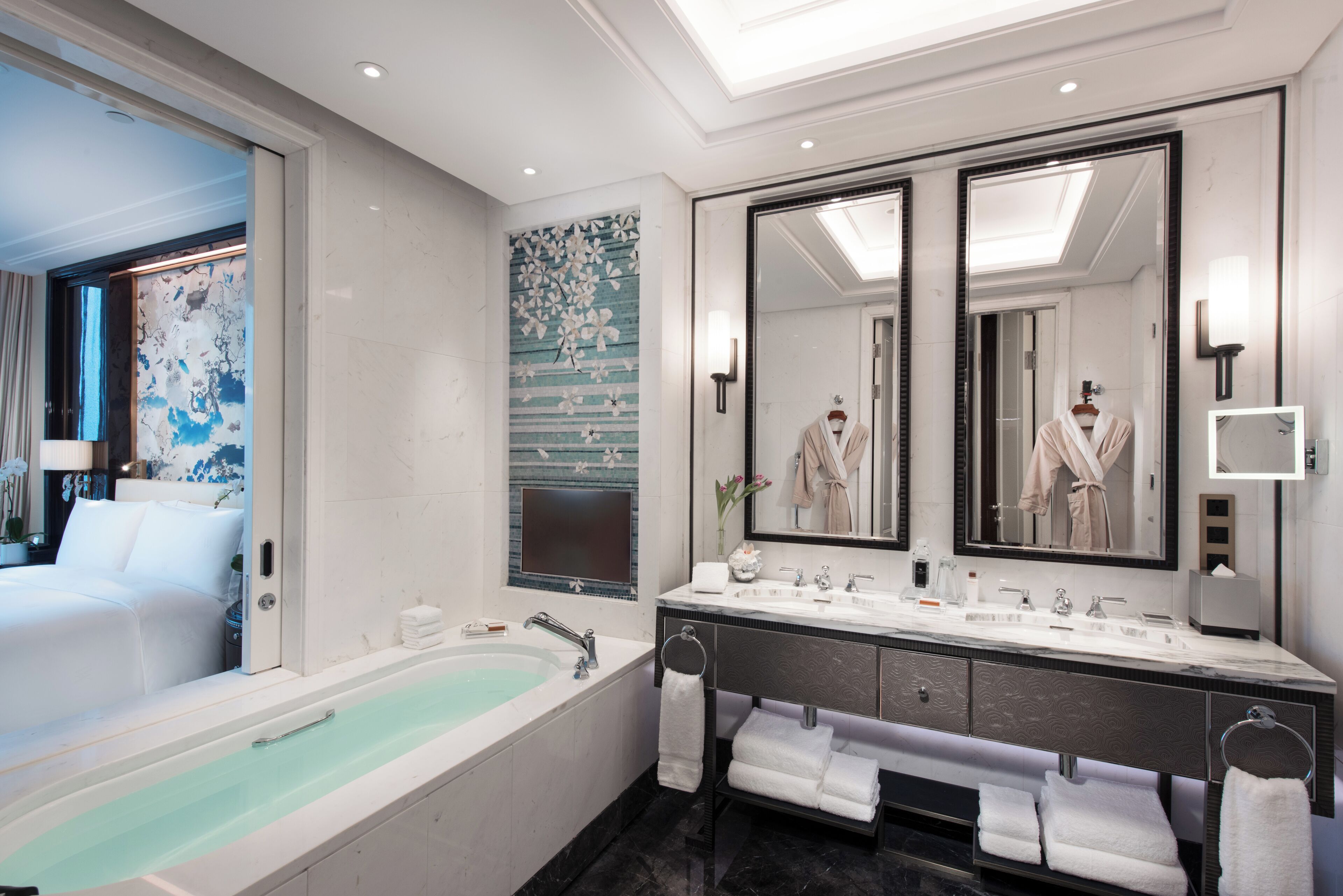 A modern bathroom with a large bathtub, dual sinks, and a large mirror.