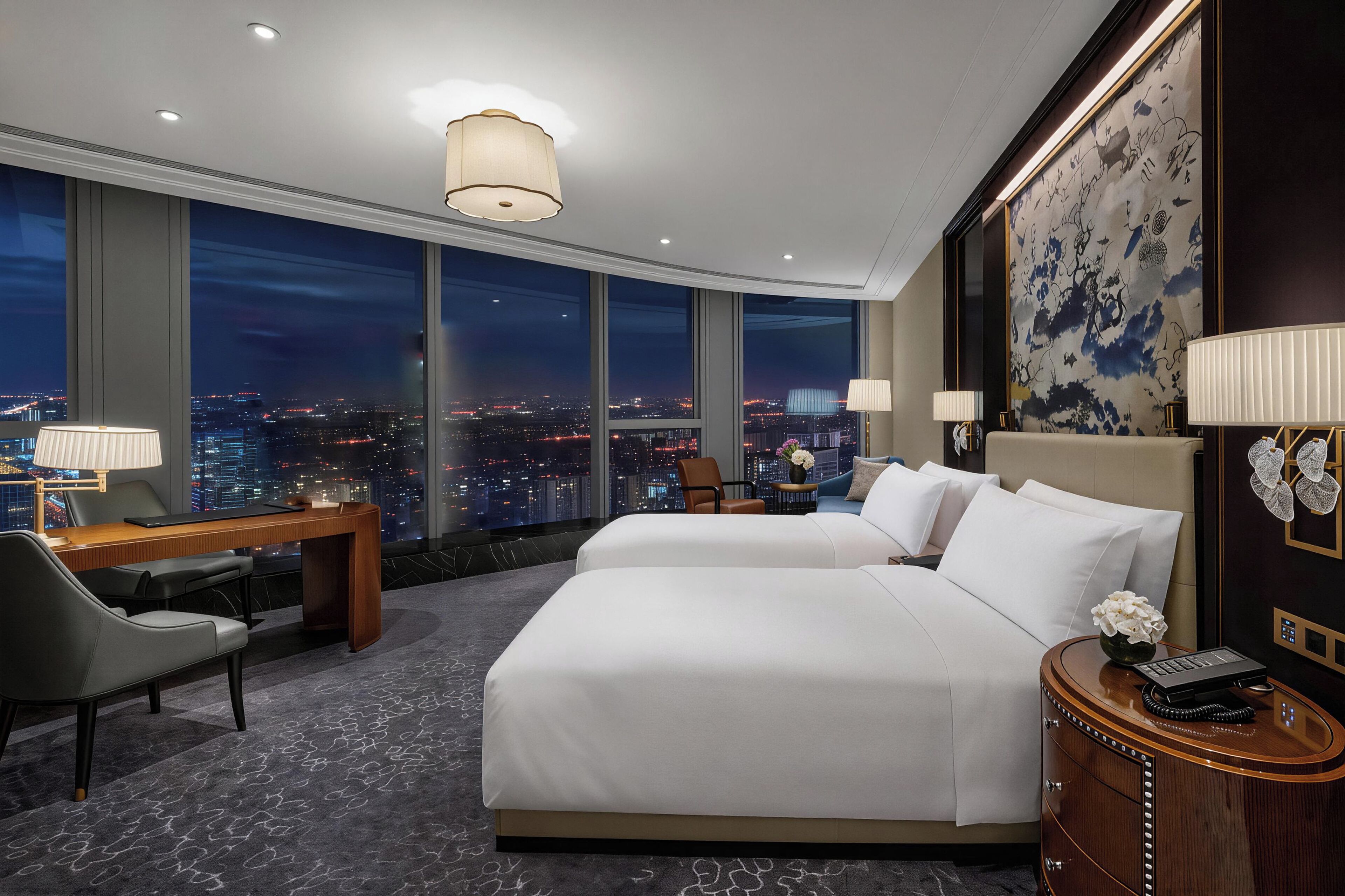 Ein Hotelzimmer mit Blick auf die Stadt, zwei Betten, einem Schreibtisch und einem Nachttisch.