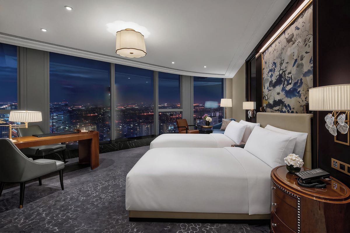A hotel room with a city view, two beds, a desk, and a nightstand.