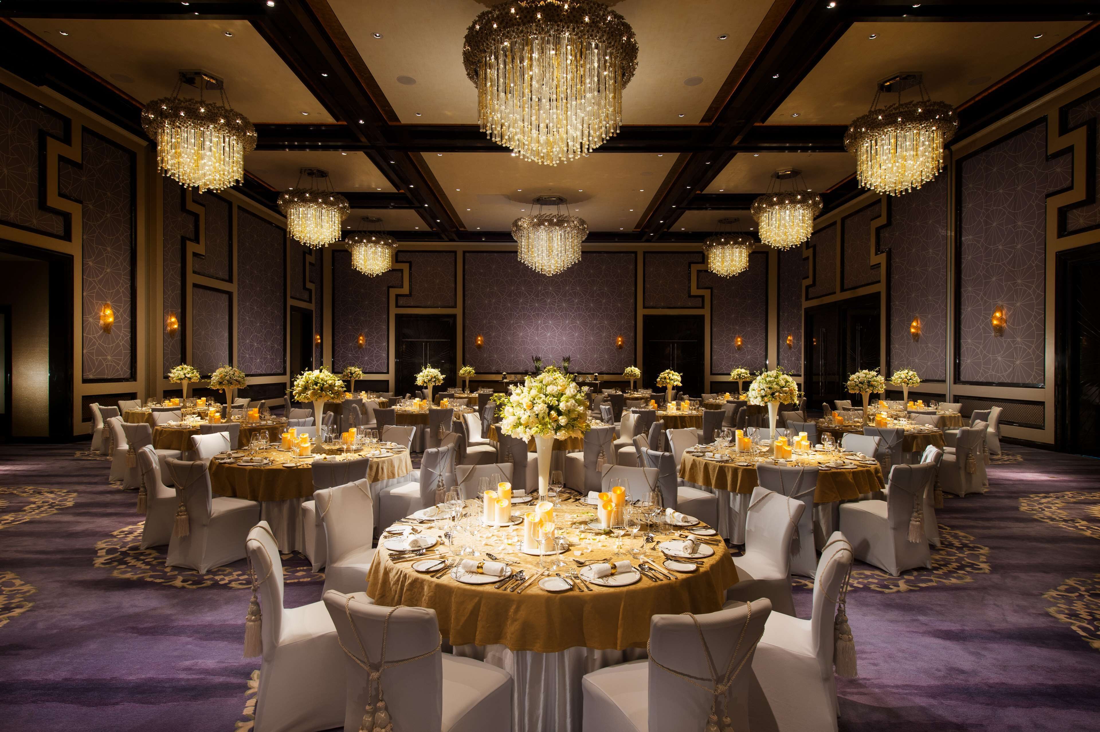 A banquet hall with round tables set for dining, large chandeliers, and floral centerpieces.