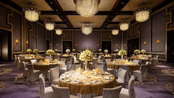 A banquet hall with round tables set for dining, large chandeliers, and floral centerpieces.