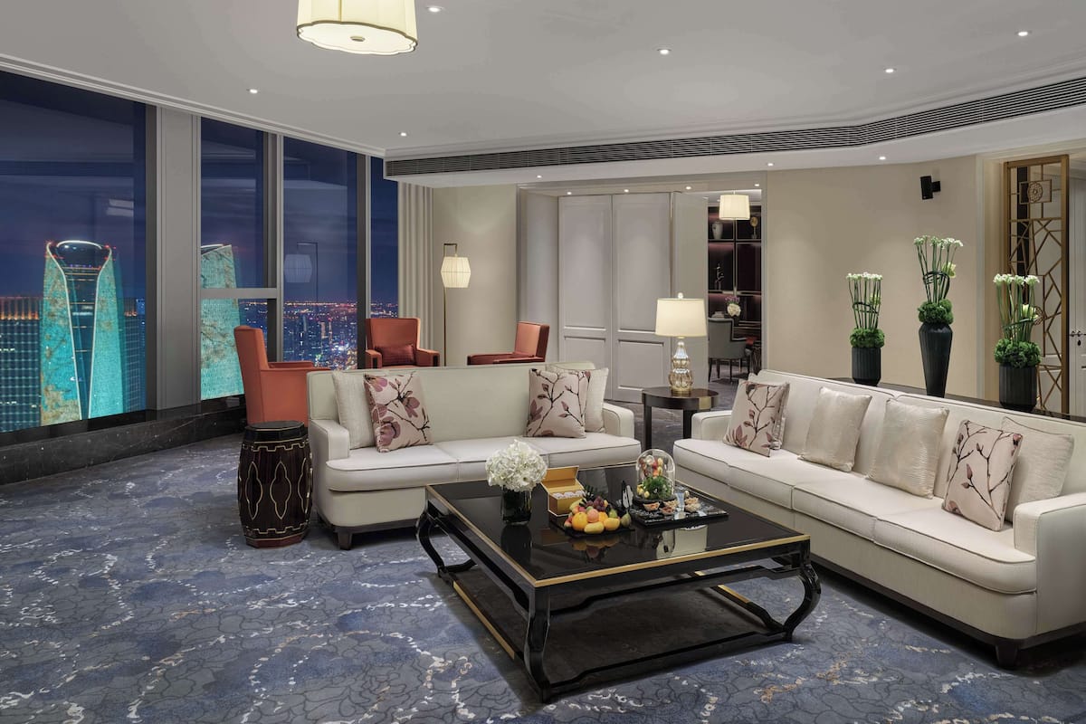 A modern living room with a large window, a sofa set, a coffee table, and decorative plants.