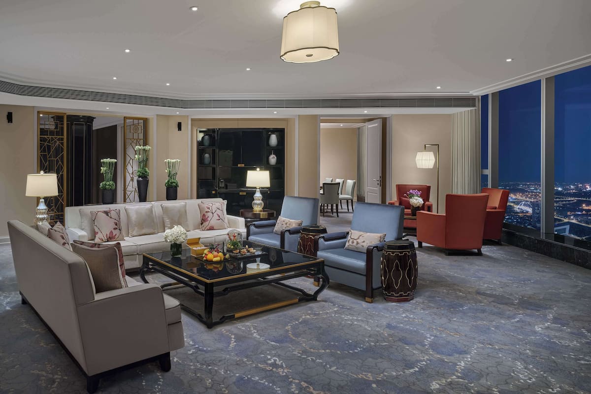 A modern hotel lobby with a sofa, chairs, a coffee table, and a large window offering a city view.