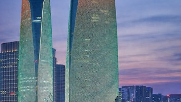 Two tall buildings with a textured facade, surrounded by a cityscape at dusk.