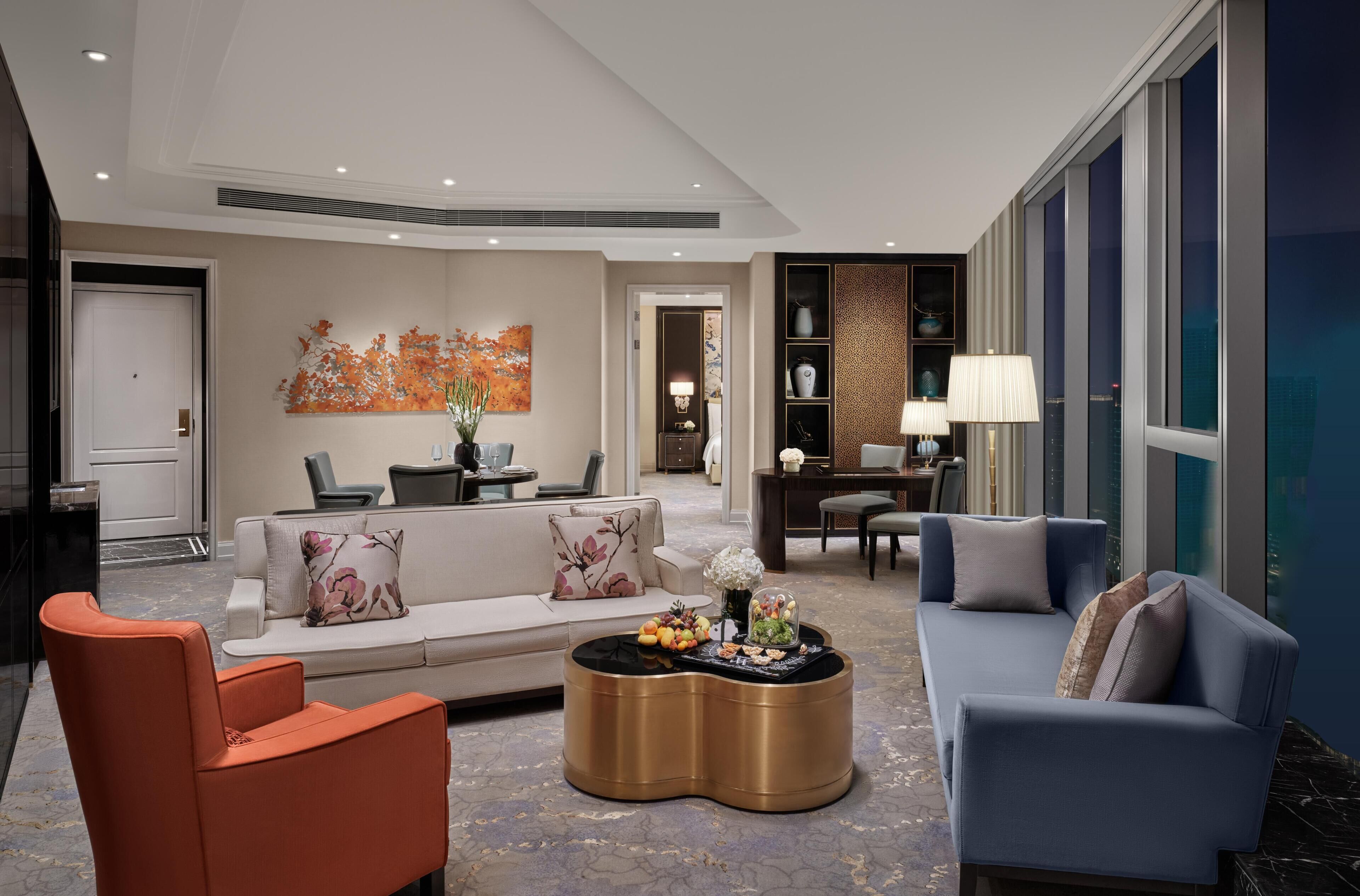 A modern hotel lobby with a sofa, armchairs, a coffee table, and a dining area.
