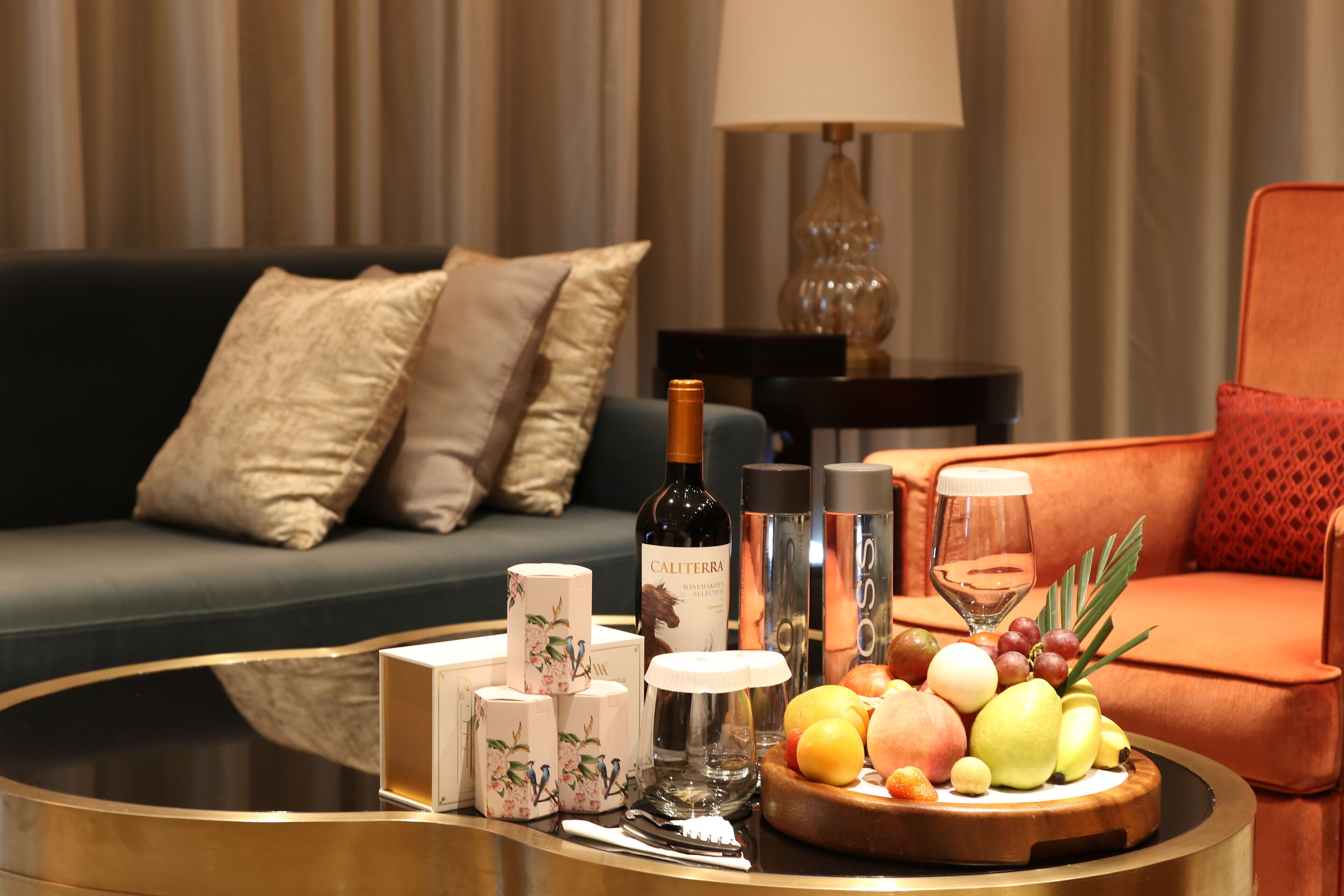 A modern living room with a round coffee table, a wine bottle, a glass, and a fruit platter.