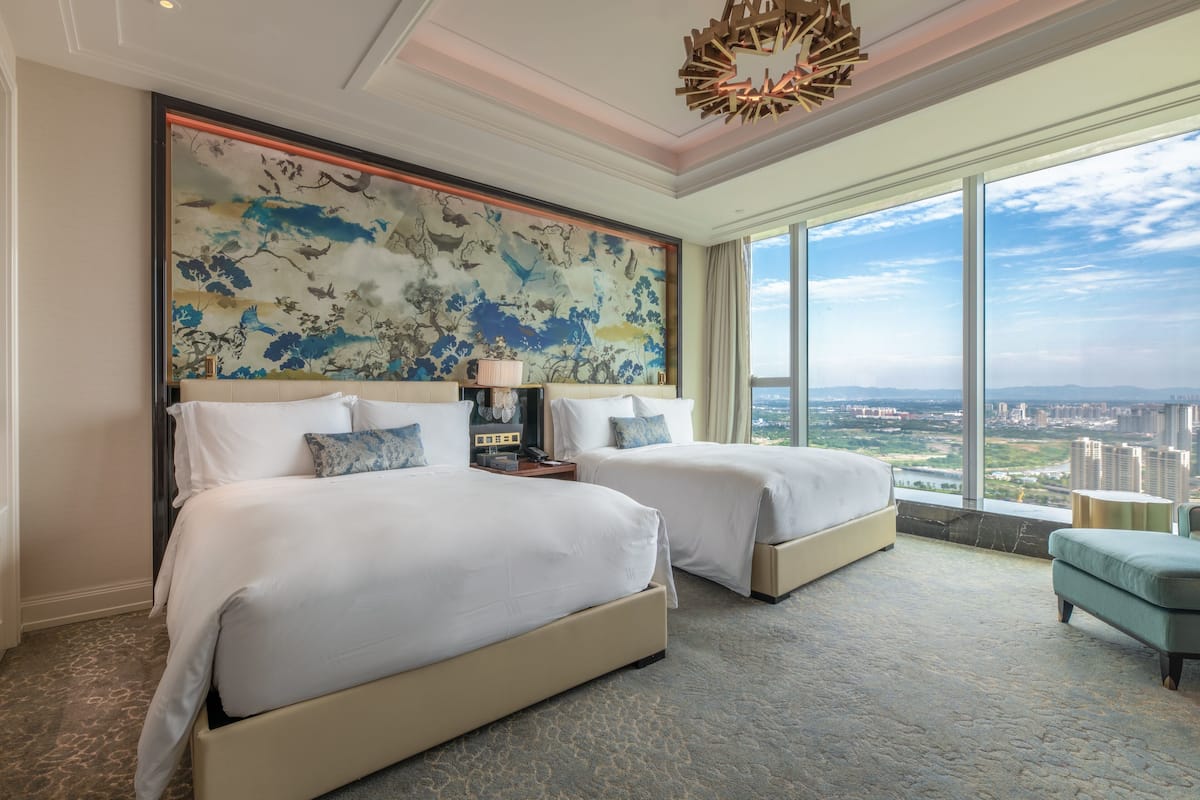 A hotel room with two beds, a large window with a city view, and a decorative wall piece.