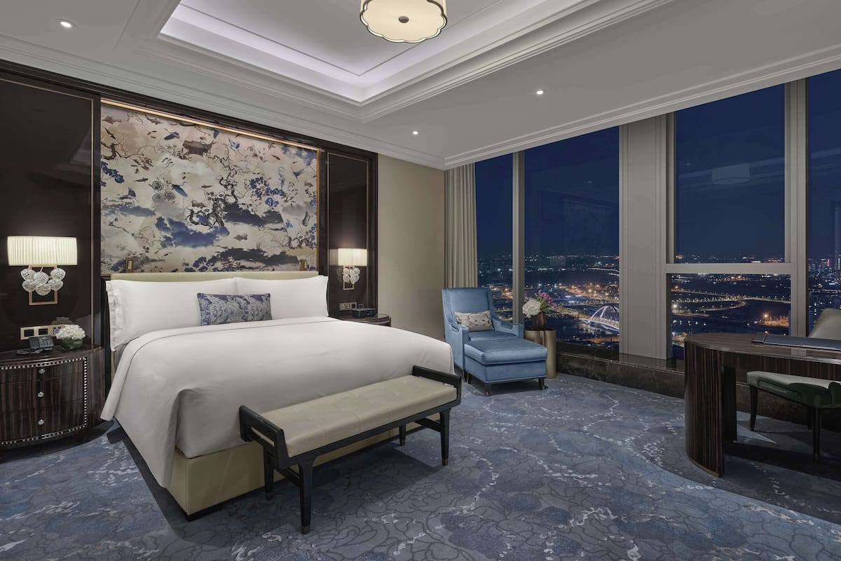 A modern hotel room with a large bed, a seating area, and a view of the city at night.