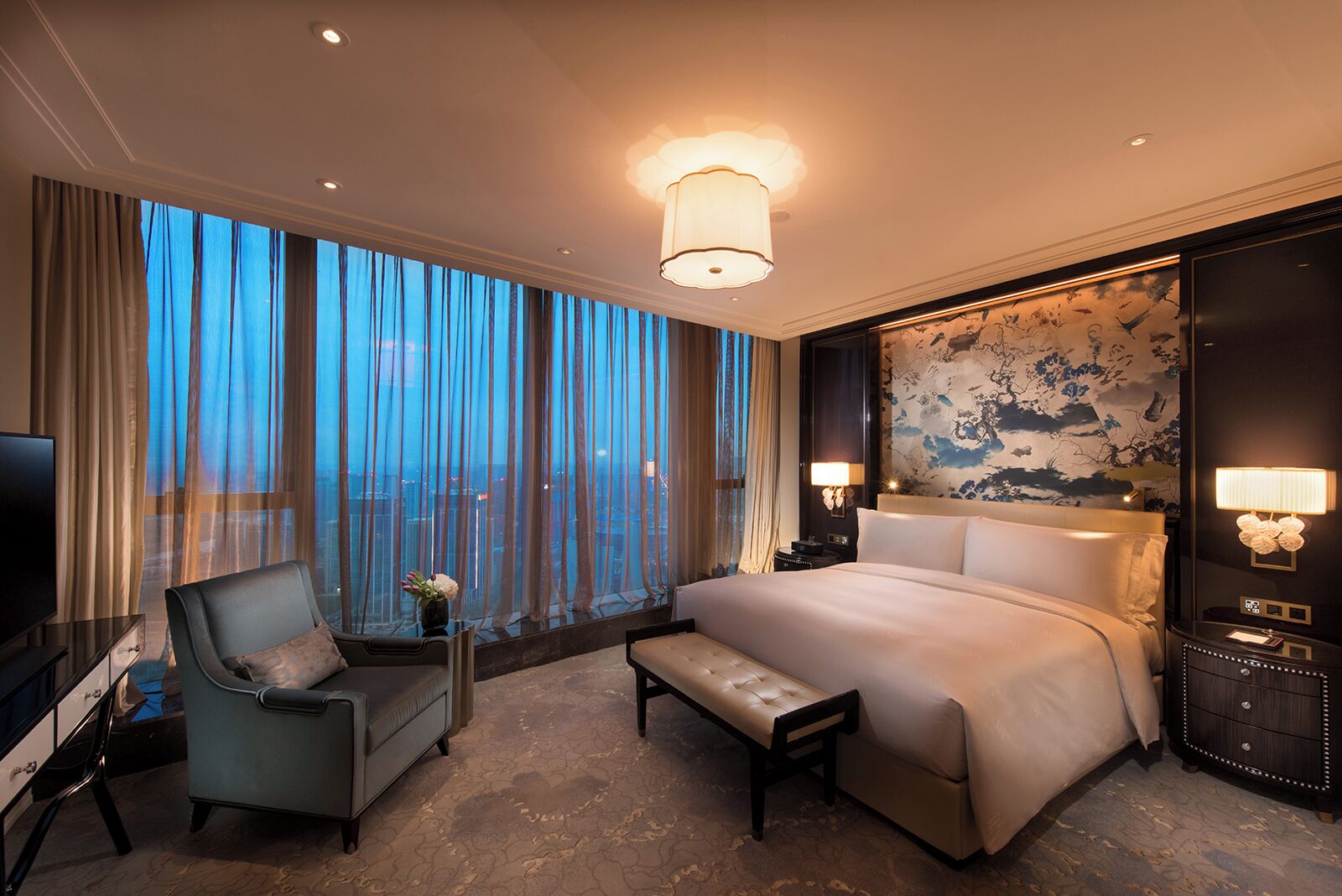 A hotel room with a large bed, a desk, a chair, and a TV.
