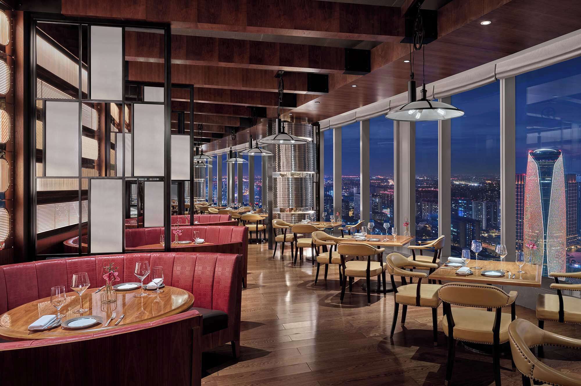 A modern restaurant with high ceilings, large windows offering city views, and a mix of seating styles including booths and tables.