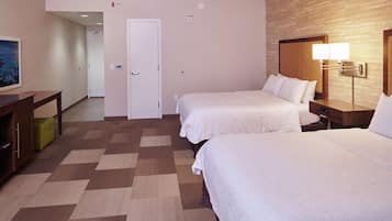A hotel room with two beds, a desk, a lamp, and a door.