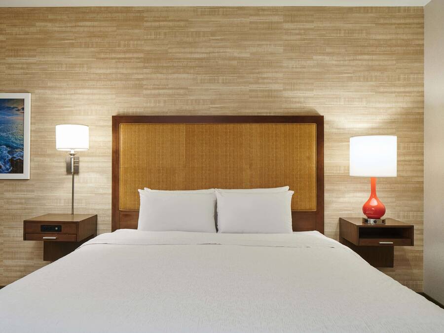 A neatly made bed with white linens, two bedside tables with lamps, and a wooden headboard.