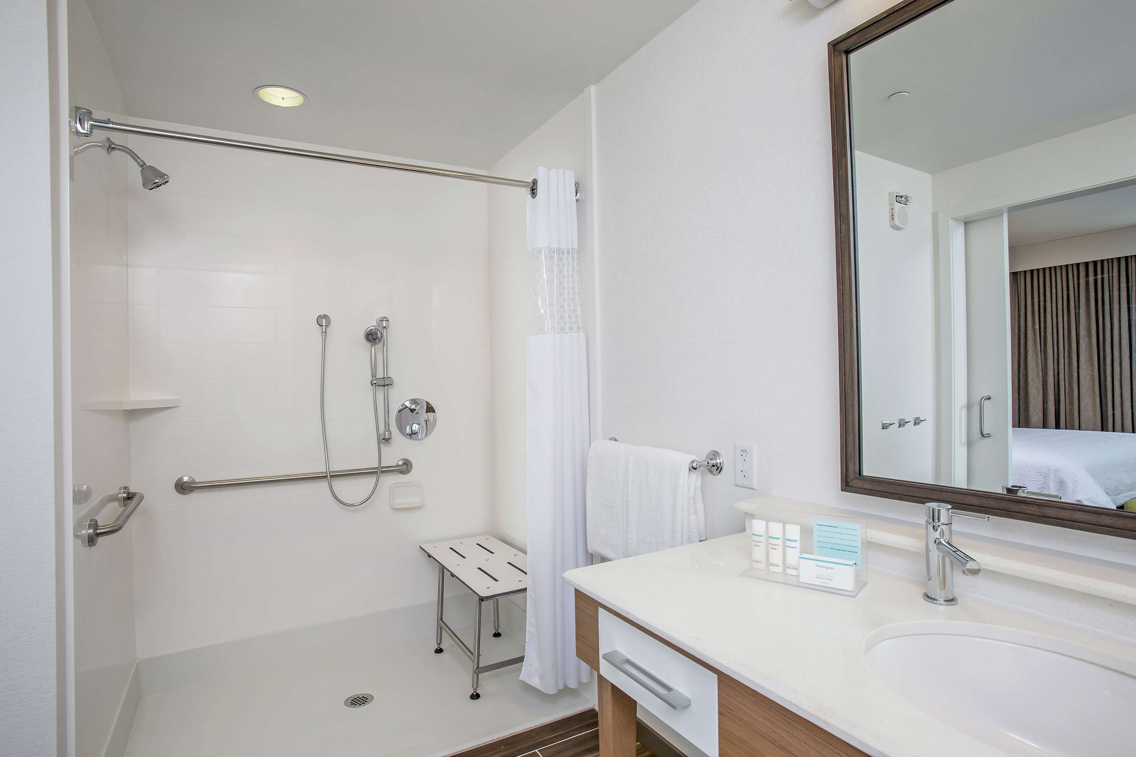 A modern bathroom with a walk-in shower, grab bars, a small vanity with a mirror, and a sink.