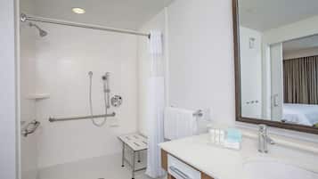 A modern bathroom with a walk-in shower, grab bars, a small vanity with a mirror, and a sink.