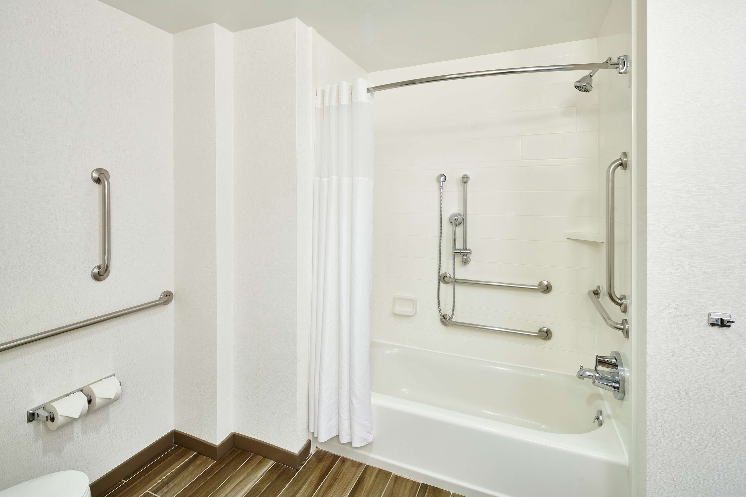 Un baño con bañera, barras de apoyo y un inodoro.
