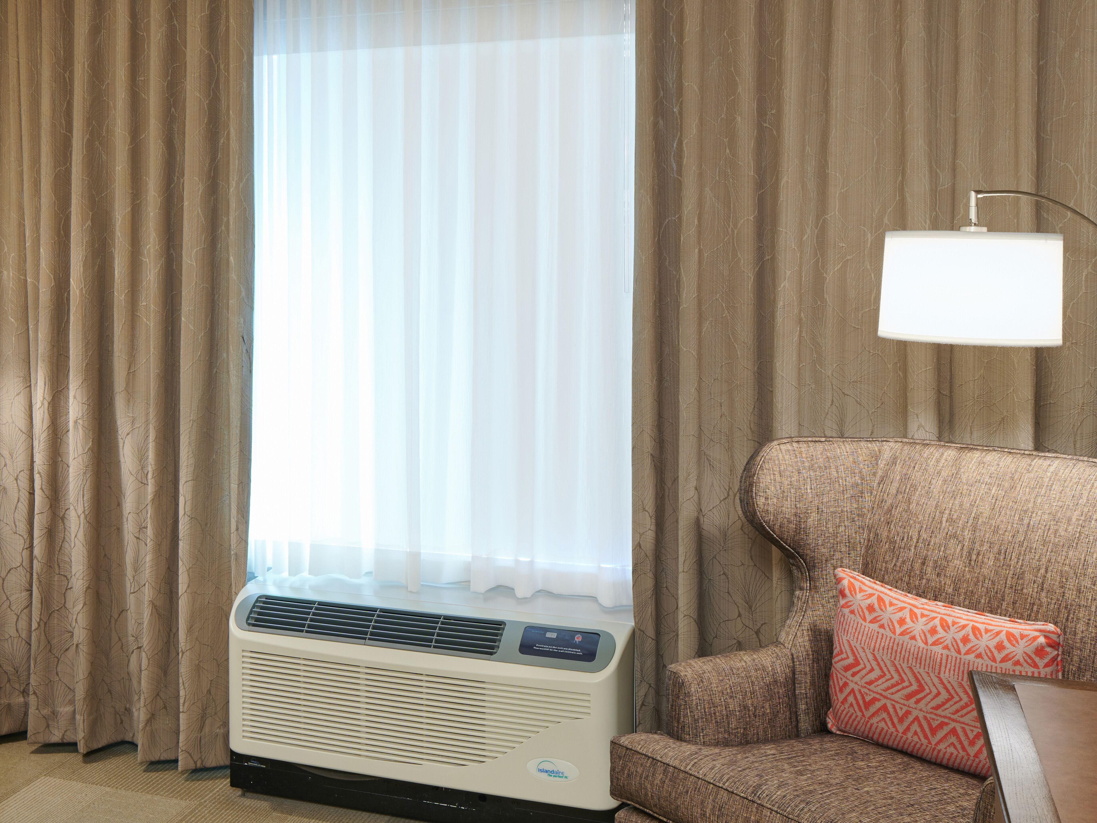 Una habitación con ventana, cortinas, aire acondicionado, sofá y una lámpara.