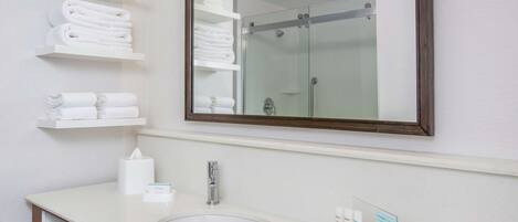 A bathroom with a large mirror, a sink, and shelves with folded towels.