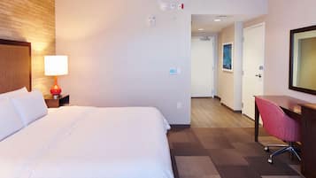 A hotel room with a large bed, a desk with a chair, a lamp, and a mirror.