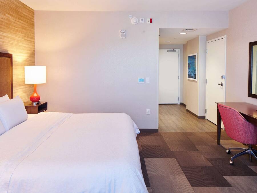 A hotel room with a large bed, a desk with a chair, a lamp, and a mirror.