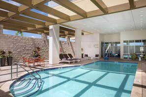 An indoor swimming pool with a clear view of the sky through the ceiling, surrounded by lounge chairs and a stone wall. - Hampton Inn & Suites Oahu/Kapolei (Kapolei)