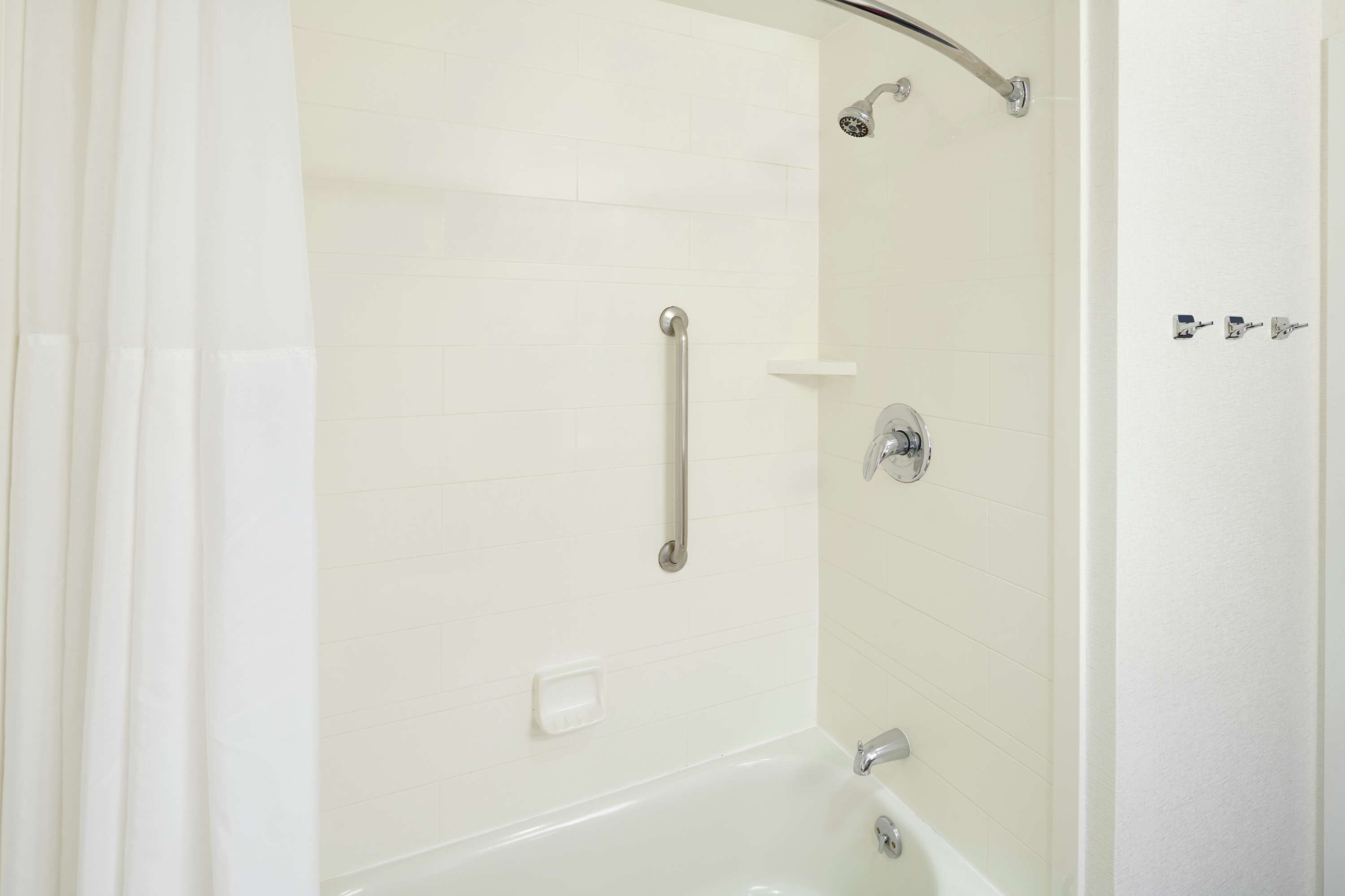 Een badkamer met een douche, een bad en een handgreep.